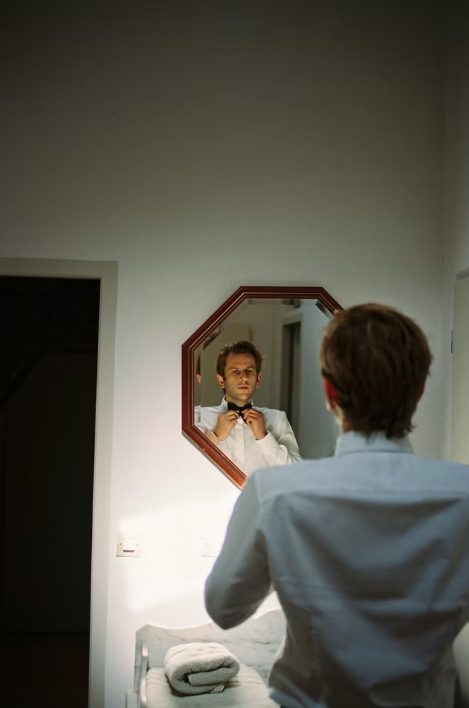 Groom adjusting his bow tie in the mirror
